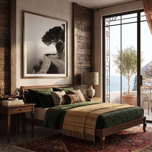 A rustic bedroom interior with a wooden bed dressed in dark green bedding and a patterned beige throw blanket, set against wood-paneled walls and a large black-and-white landscape print. A large glass sliding door reveals an outdoor balcony and coastal town view, with brown curtains, a patterned rug, and wooden nightstands.