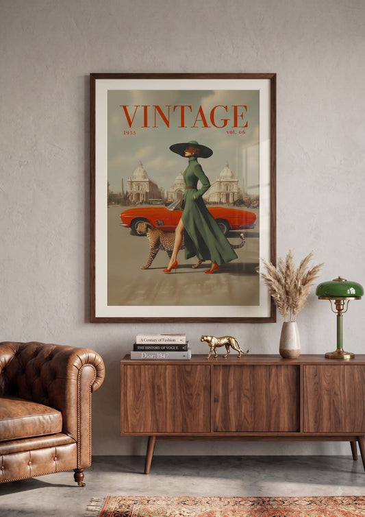 A framed vintage-style poster hangs on a light gray wall above a wooden sideboard in a styled room. The poster features the word 'VINTAGE' at the top, an orange car, a woman in a long green dress and black hat, and a dog.