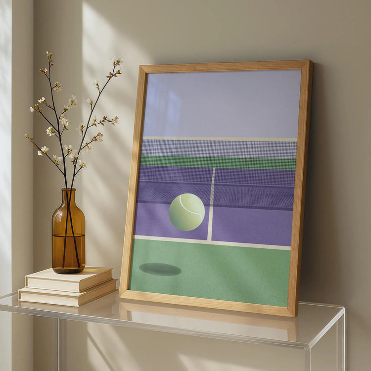 Framed artwork of a tennis court with a ball on a table next to a vase and books.Modern minimalist illustration of a tennis ball mid-bounce on a textured court with a soft pastel sky background