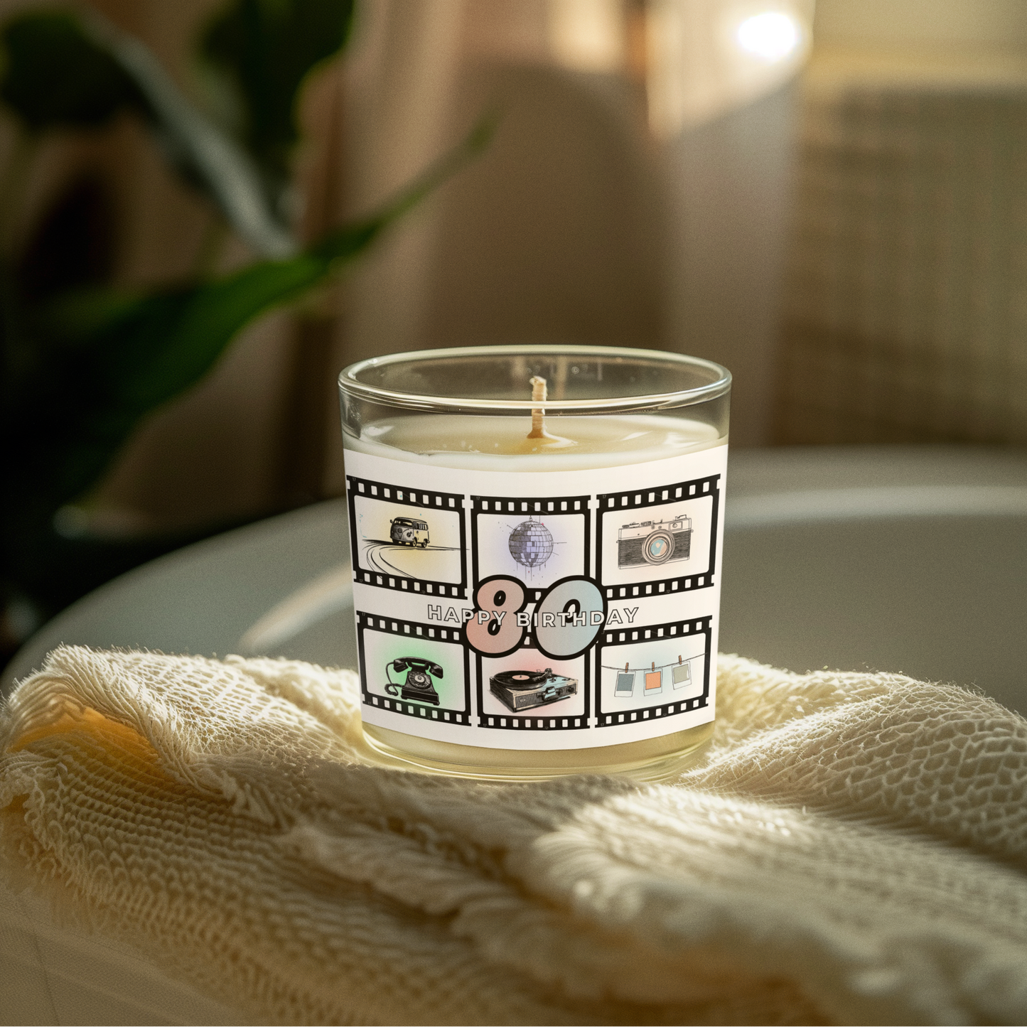 Candle with a 'Happy Birthday' '80' -themed label on a white surface with a plant in the background