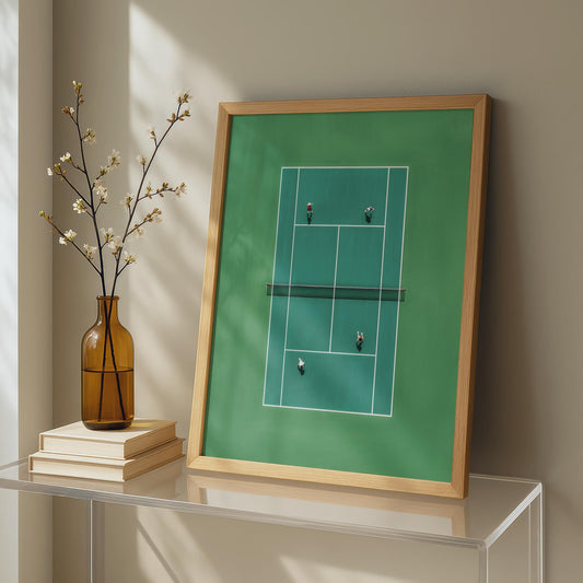 Framed artwork of a tennis court in miniature from above on a table with a vase and books.
