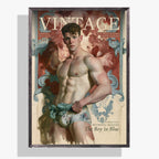 A framed vintage-style poster or print featuring a muscular male model with the large word 'VINTAGE' across the top and additional text including 'The Boy in Blue'. The artwork has a cream background with red, blue, and flesh-toned imagery, and the piece is shown hanging against a light gray wall.