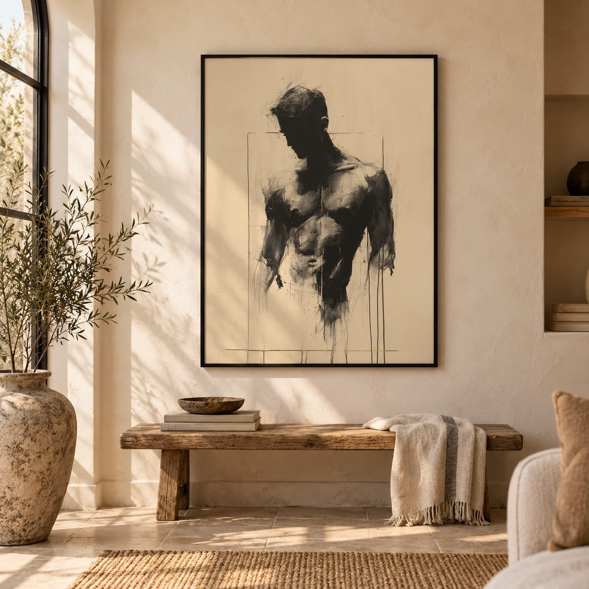 Bare Masculinity male figure print in a black frame on a warm cream wall above a rustic wooden bench, with a jute rug, olive tree and large vase.