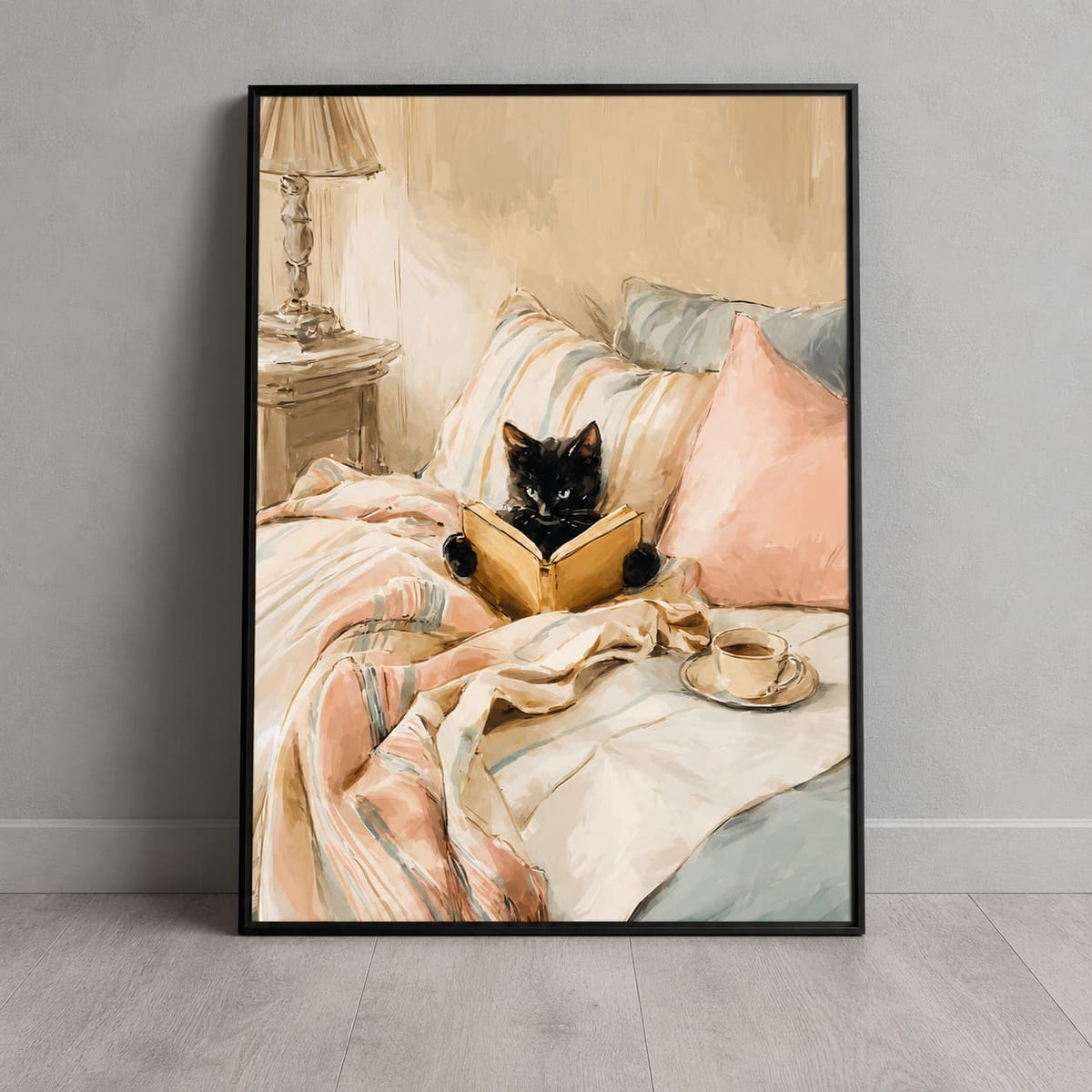 Framed black cat reading print leaning against a light grey wall, showing blush pink bedding, a glowing lamp and a cup of tea.
