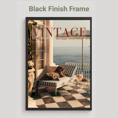A framed vintage-style poster or print hanging on a light gray wall, with the text 'Black Finish Frame' above it. The artwork shows a sunlit balcony scene with a striped lounge chair, leopard print cushion, ocean view, and large 'VINTAGE' lettering across the top.