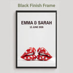 A framed personalized wall art print with a black frame, featuring the text 'EMMA & SARAH 12 JUNE 2026' above a pair of red lips with white polka dots, shown on a light gray background with the text 'Black Finish Frame' above.