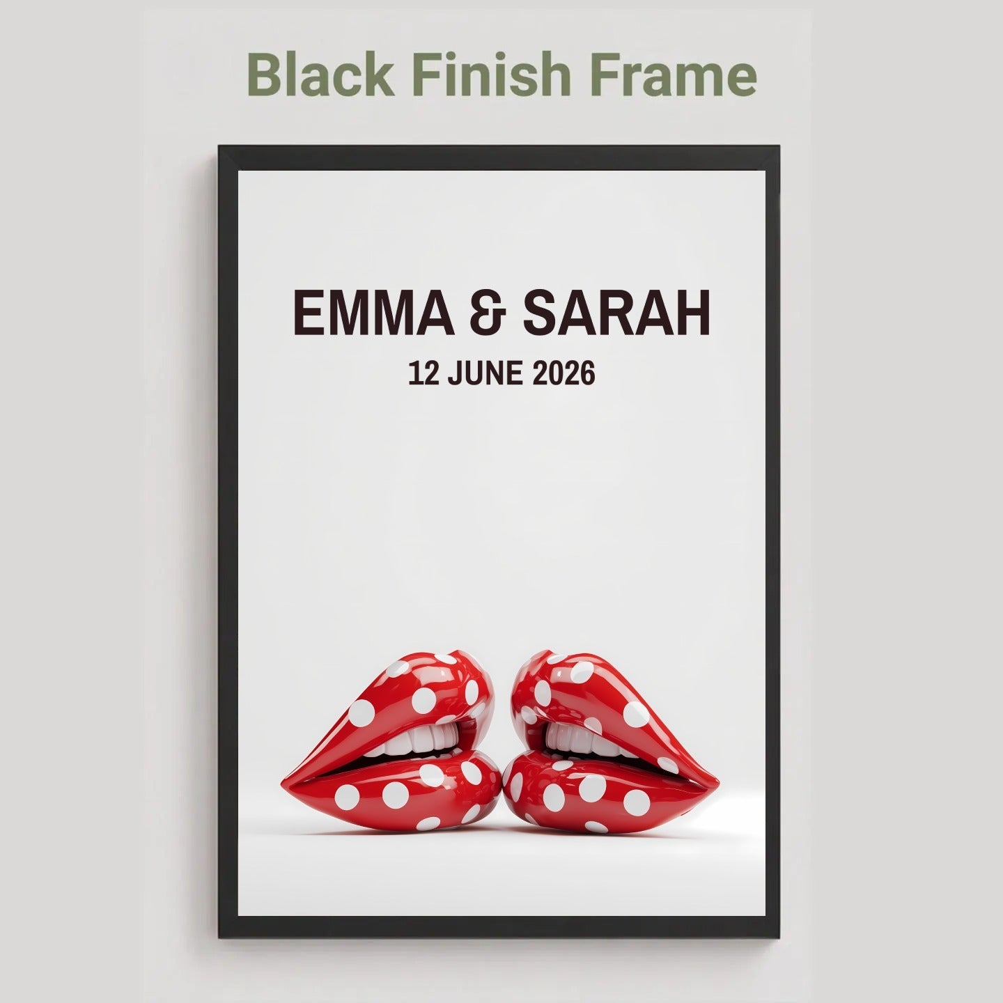 A framed personalized wall art print with a black frame, featuring the text 'EMMA & SARAH 12 JUNE 2026' above a pair of red lips with white polka dots, shown on a light gray background with the text 'Black Finish Frame' above.