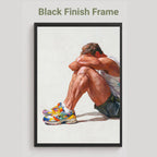 Rest gay art print in the black finish frame option, a seated man resting his head on his knees in colourful trainers, labelled Black Finish Frame