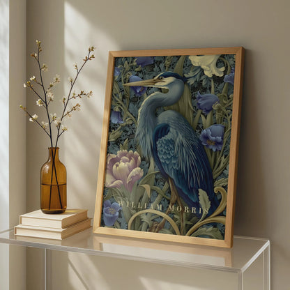 Framed artwork of a blue heron among flowers on a shelf with a vase and books. Blue heron among peonies and campanula in Victorian Arts & Crafts botanical style — dark teal, navy and olive art print