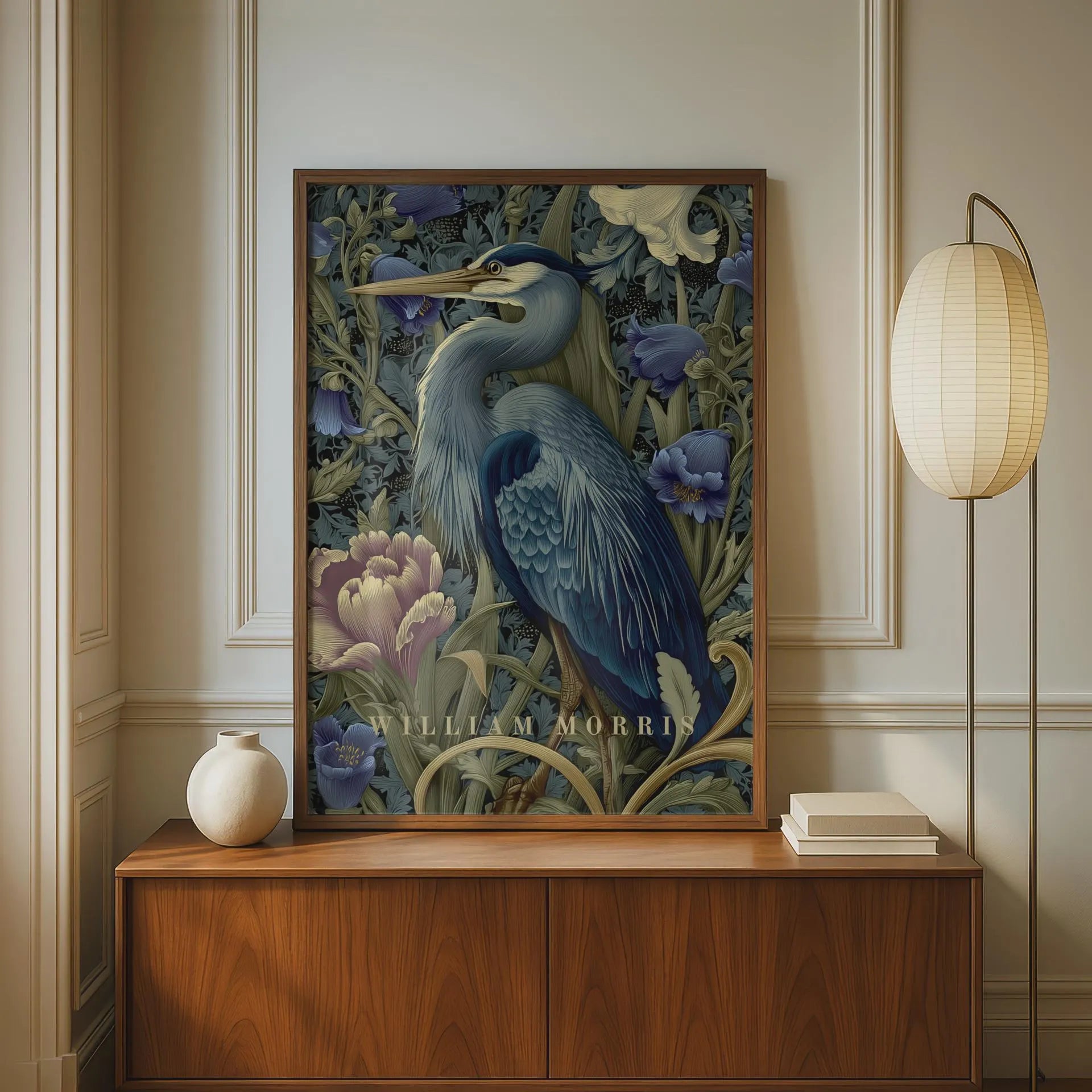 Framed artwork of a heron with floral elements on a wall above a wooden cabinet. Blue heron among peonies and campanula in Victorian Arts & Crafts botanical style — dark teal, navy and olive art print