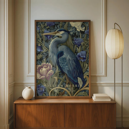 Framed artwork of a heron with floral elements on a wall above a wooden cabinet. Blue heron among peonies and campanula in Victorian Arts & Crafts botanical style — dark teal, navy and olive art print