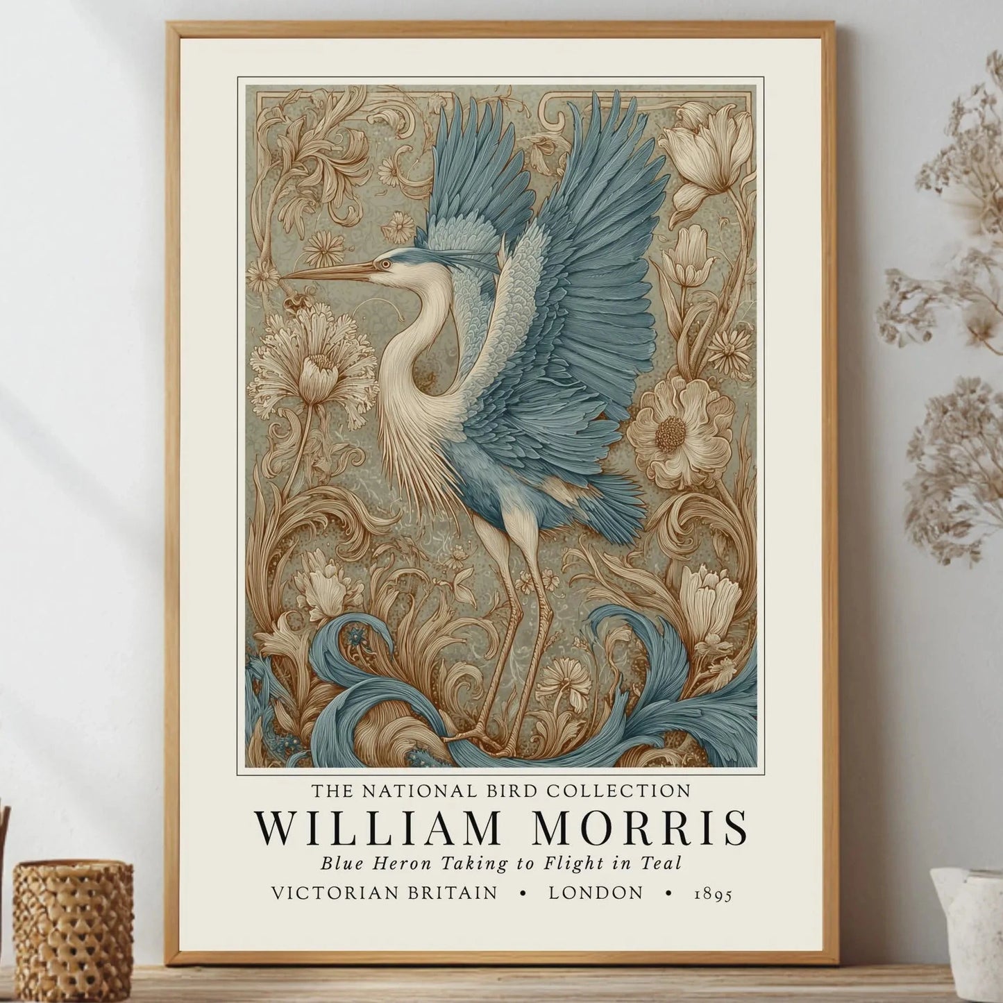 Framed artwork of a blue heron with floral elements on a wall. William Morris style exhibition poster featuring a blue heron taking to flight, surrounded by ornate acanthus scrolls, dahlias and botanical foliage in teal, gold and antique cream — Arts & Crafts wall art print