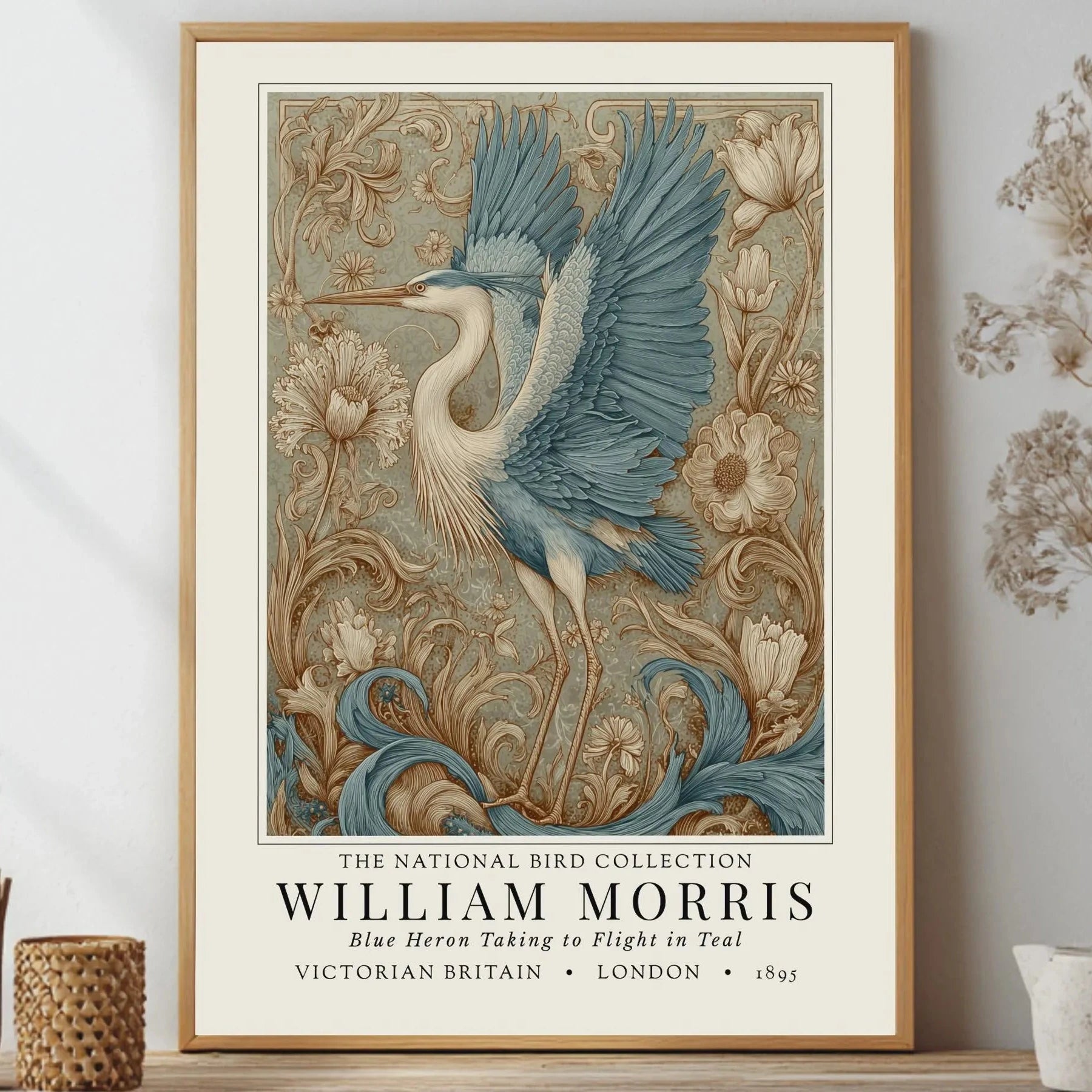 Framed artwork of a blue heron with floral elements on a wall. William Morris style exhibition poster featuring a blue heron taking to flight, surrounded by ornate acanthus scrolls, dahlias and botanical foliage in teal, gold and antique cream — Arts & Crafts wall art print
