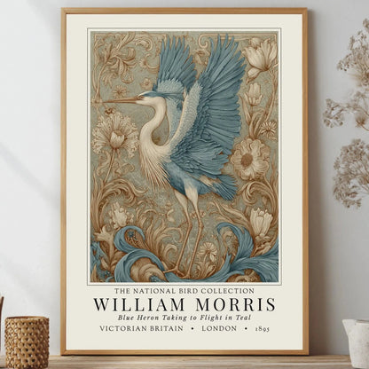 Framed artwork of a blue heron with floral elements on a wall. William Morris style exhibition poster featuring a blue heron taking to flight, surrounded by ornate acanthus scrolls, dahlias and botanical foliage in teal, gold and antique cream — Arts & Crafts wall art print