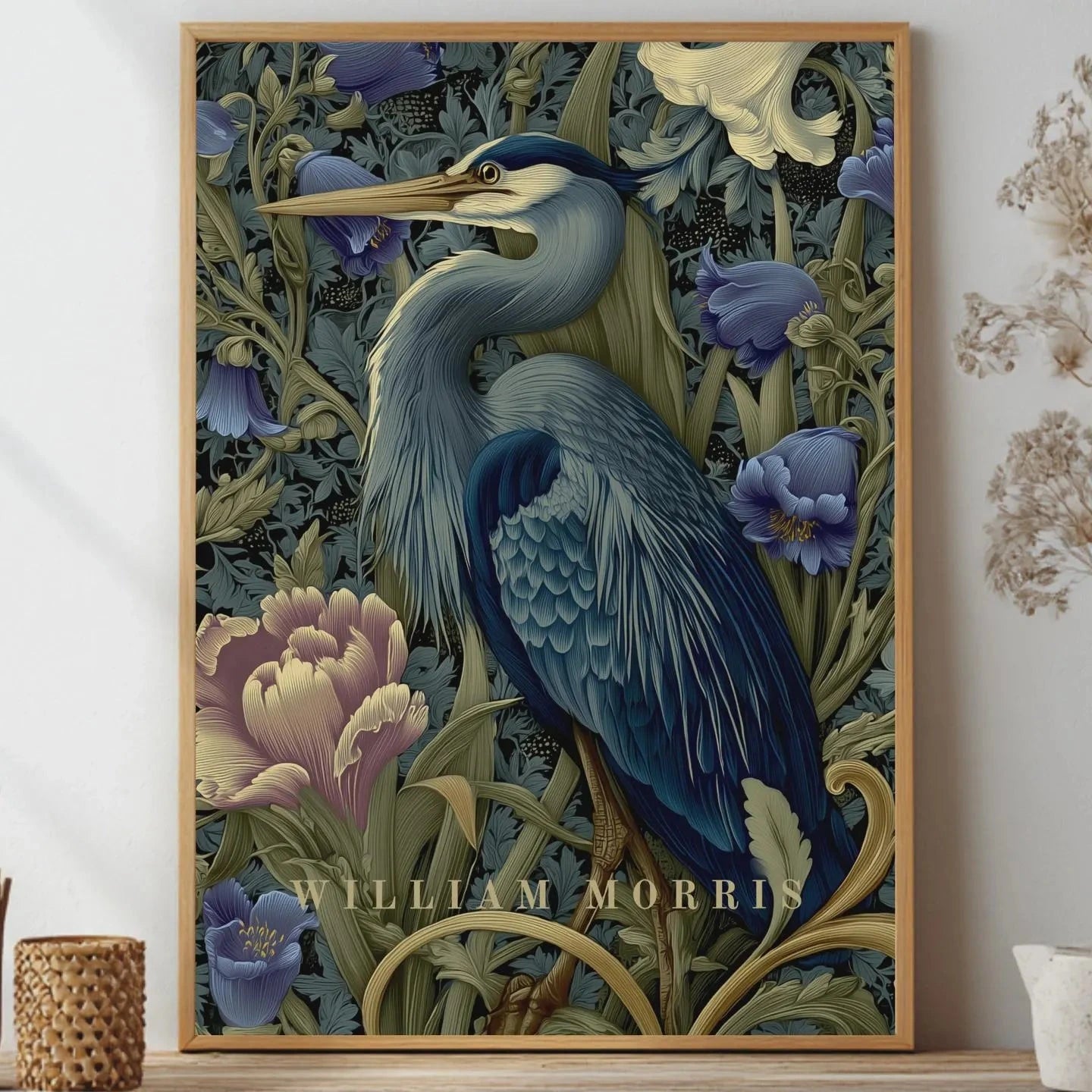 Framed artwork of a heron among flowers with 'William Morris' branding, displayed on a wall. Blue heron among peonies and campanula in Victorian Arts & Crafts botanical style — dark teal, navy and olive art print