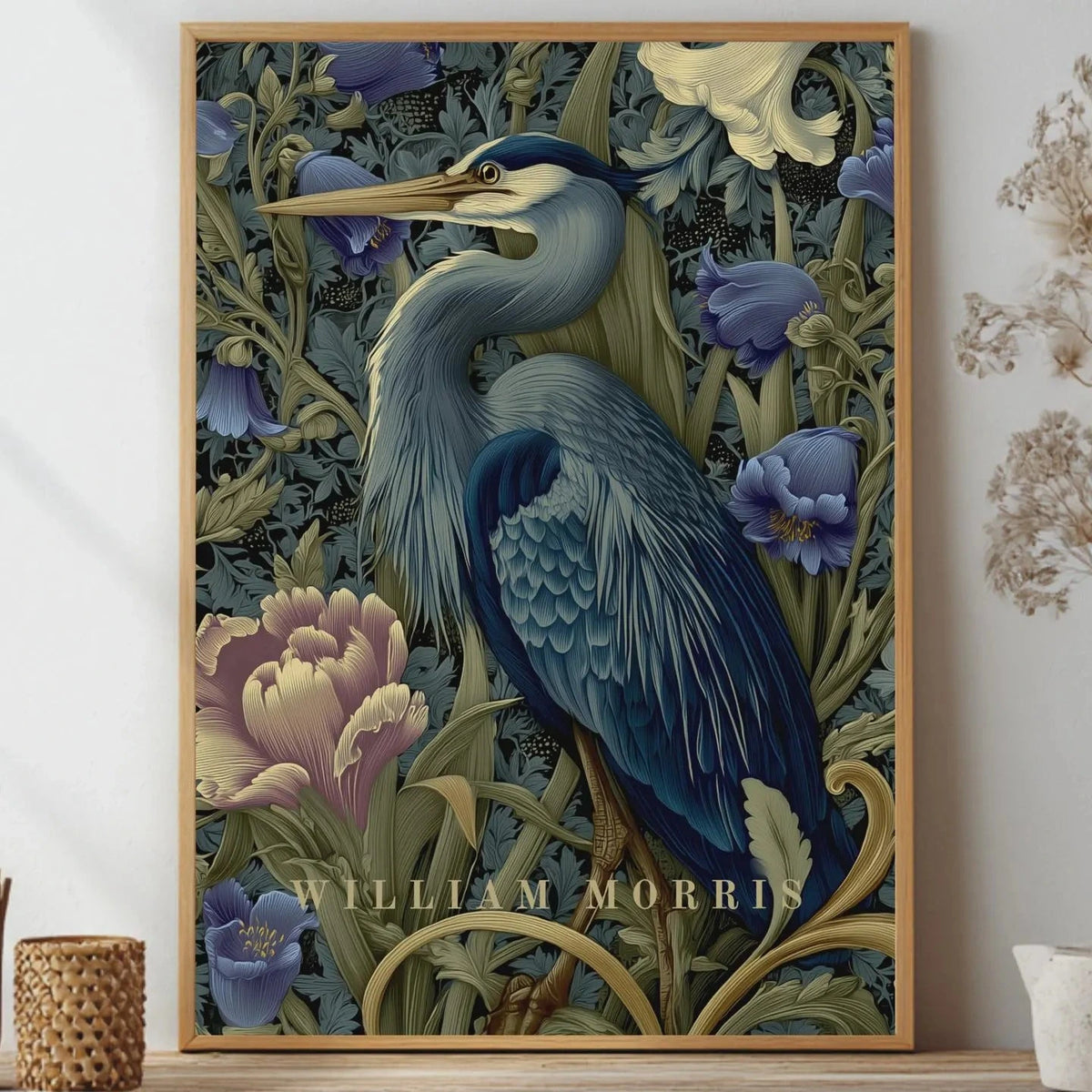 Framed artwork of a heron among flowers with 'William Morris' branding, displayed on a wall. Blue heron among peonies and campanula in Victorian Arts & Crafts botanical style — dark teal, navy and olive art print