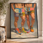 A framed art print leaning against a white wall on a beige rug, showing a painted scene of two men's lower torsos and legs wearing colorful patchwork shorts and sneakers.
