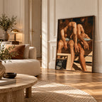A large framed art print depicting two nude men seated on a bench, leaning against a cream paneled wall in a sunlit, elegant living room with a beige sofa and wood floors.