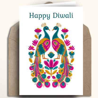 A white greeting card with the text 'Happy Diwali' above a colorful symmetrical peacock illustration, shown with a brown kraft envelope behind it on a light beige background.