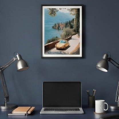 Framed artwork of a scenic coastal road with a car, displayed above a desk with a laptop and office items.