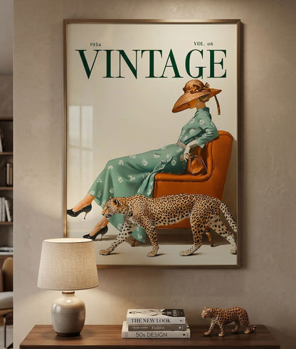 Framed artwork of a woman in a vintage setting with a leopard on a wall above a wooden console table. 1950s vintage magazine cover poster featuring a woman in a sage green floral dress and wide-brimmed hat seated on a burnt orange leather chair, with a cheetah walking alongside her, forest green VINTAGE typography on cream background