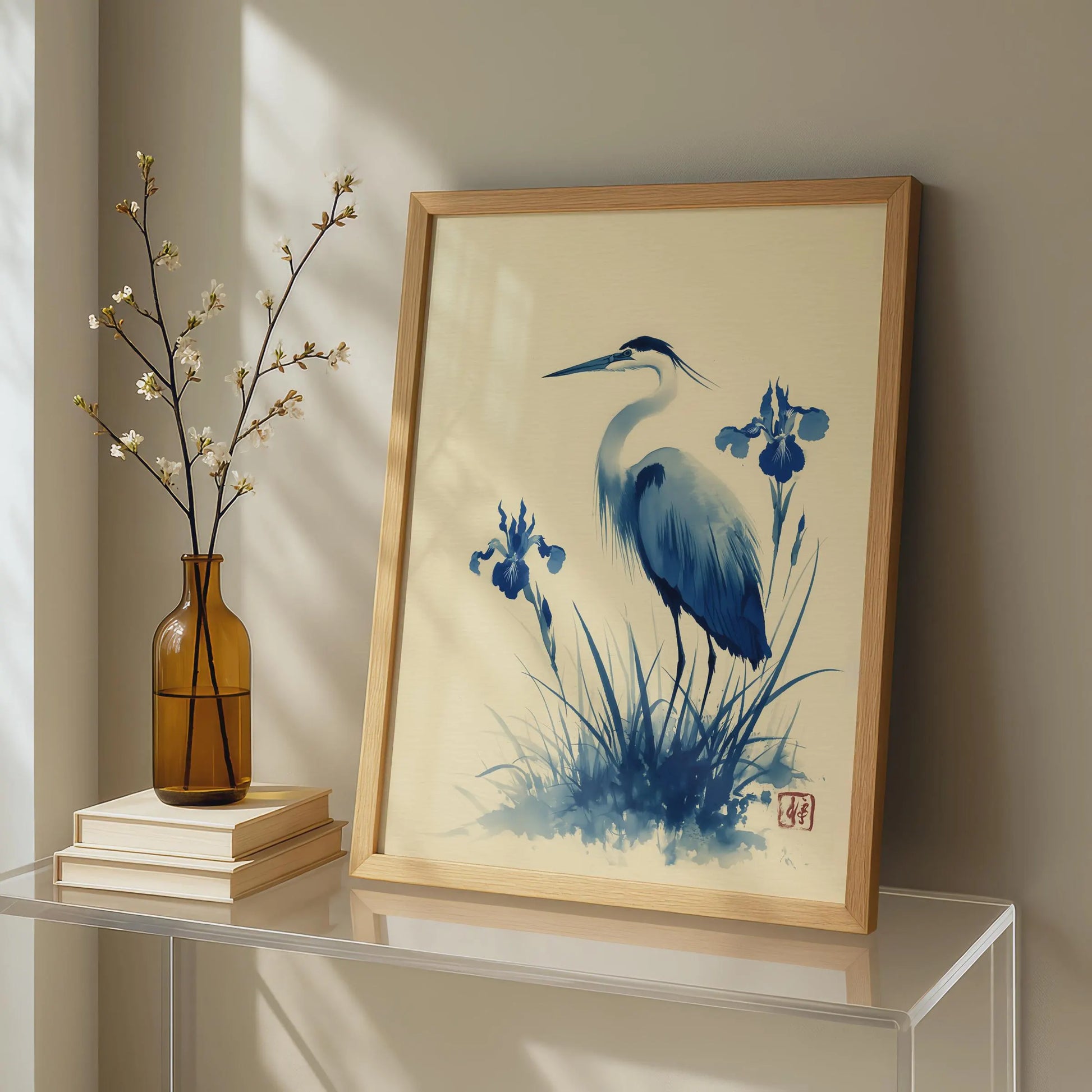 Framed artwork of a blue heron and iris flowers on a shelf with a vase and books.Blue heron and water iris sumi-e print in indigo and cream — Japanese watercolour wall art with cinnabar seal