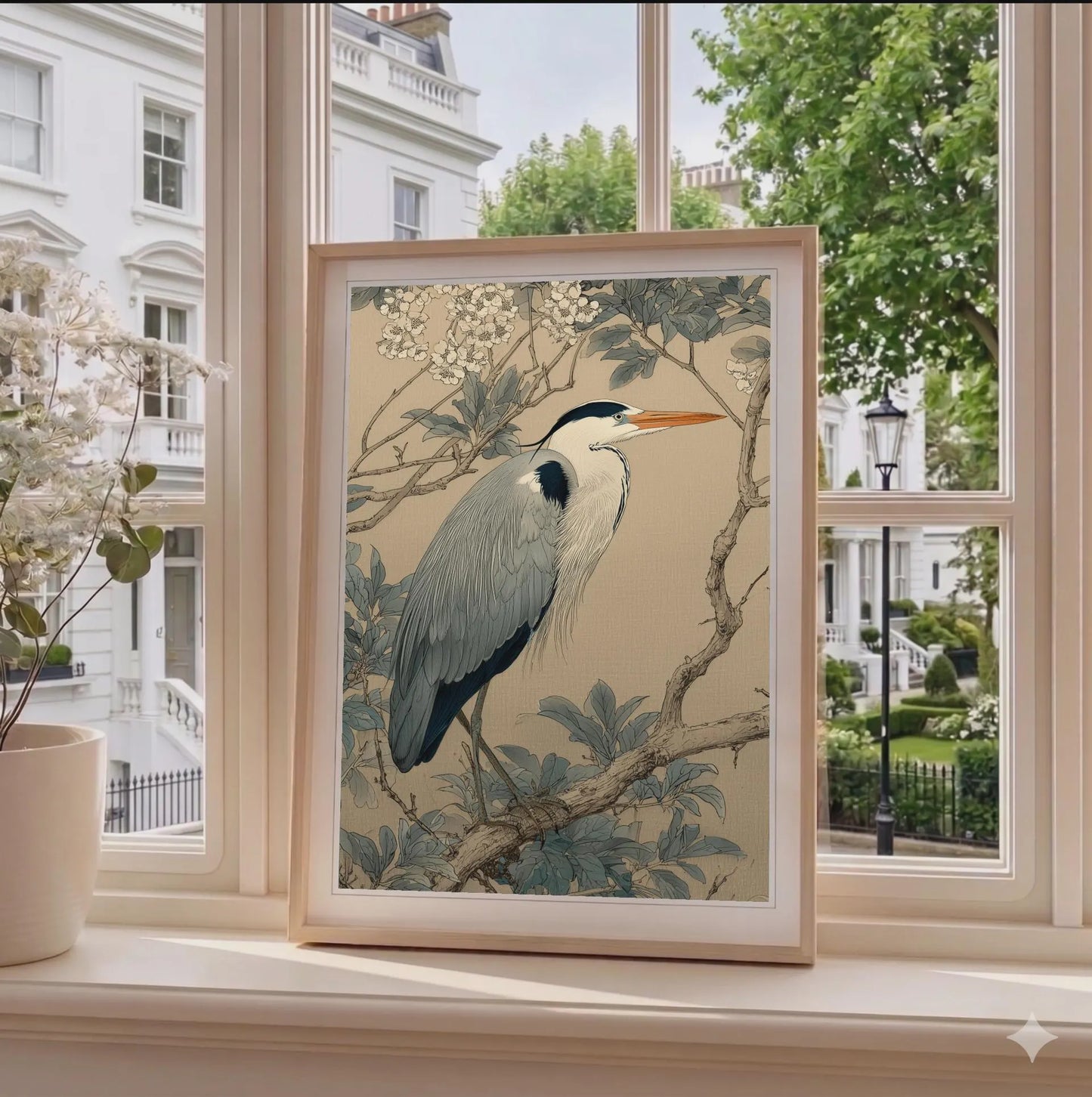 Framed artwork of a heron on a branch with flowers, displayed by a window.