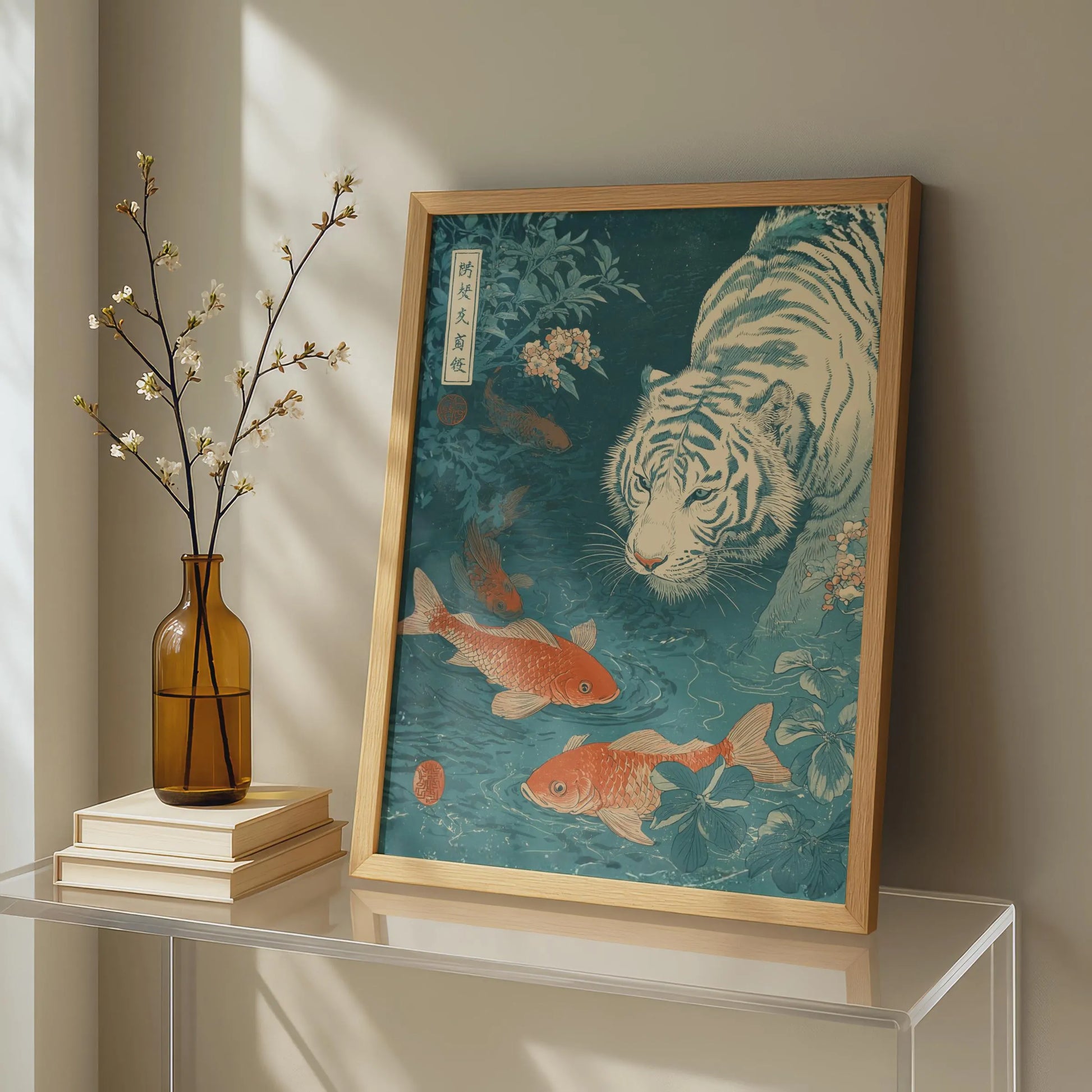 Framed artwork of a tiger and goldfish on a shelf with a vase and books. Japanese woodblock-style art print of a white tiger gazing into a teal koi pond, with three orange koi fish swimming in the foreground, cherry blossoms, lush foliage, and traditional Japanese calligraphy seals, in a deep teal and burnt-orange palette.