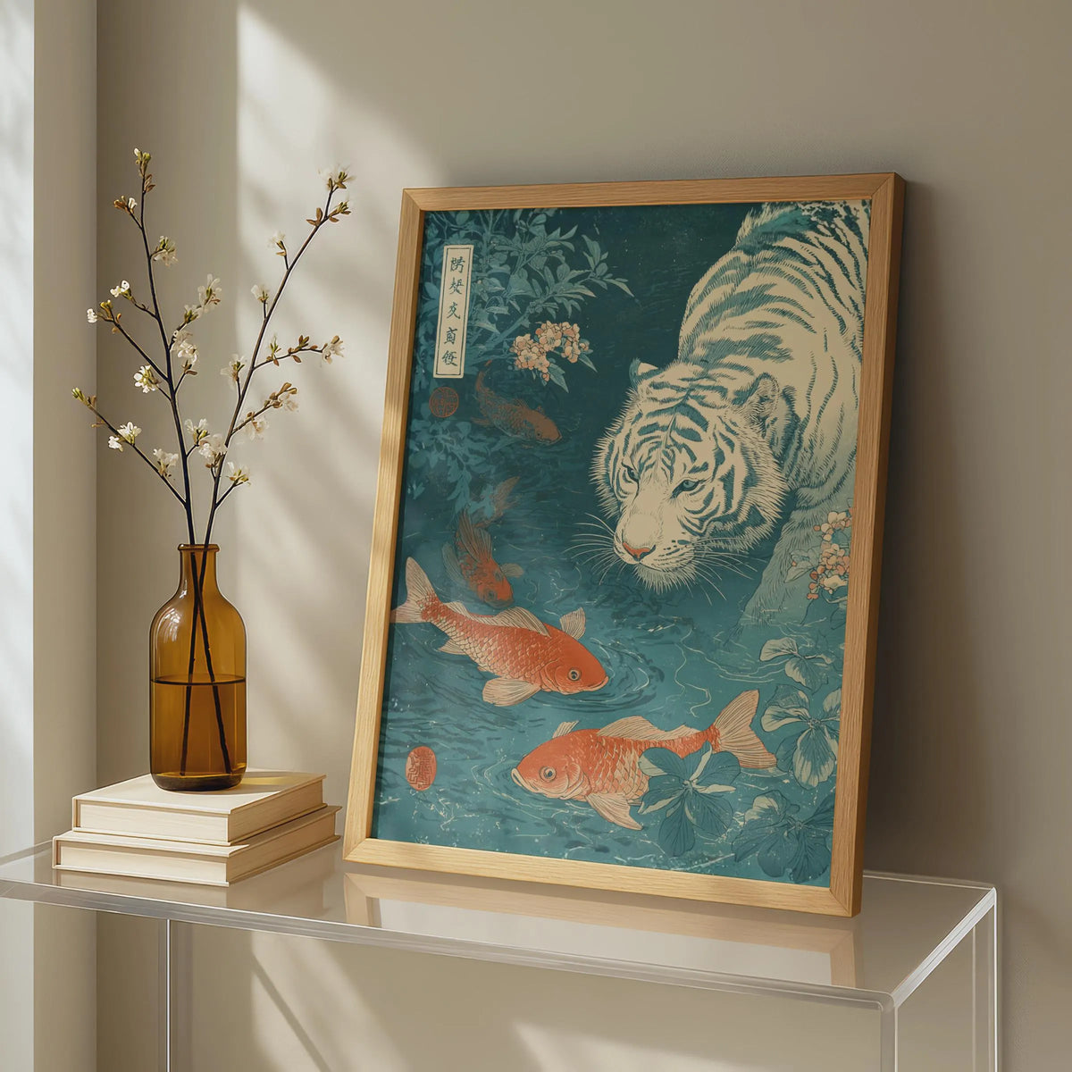 Framed artwork of a tiger and goldfish on a shelf with a vase and books. Japanese woodblock-style art print of a white tiger gazing into a teal koi pond, with three orange koi fish swimming in the foreground, cherry blossoms, lush foliage, and traditional Japanese calligraphy seals, in a deep teal and burnt-orange palette.