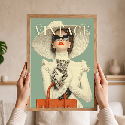 A person holds a framed vintage-style art print featuring a woman in a large hat and sunglasses holding a leopard cub, with the text 'VINTOIRE' and '1959 vol. 04' on a mint background.