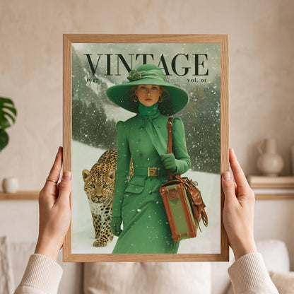 A person holds a framed vintage-style art print featuring a woman in a green outfit and hat walking with a leopard in the snow. The print has the word "VINTAGE" at the top and is shown against a softly lit indoor background.