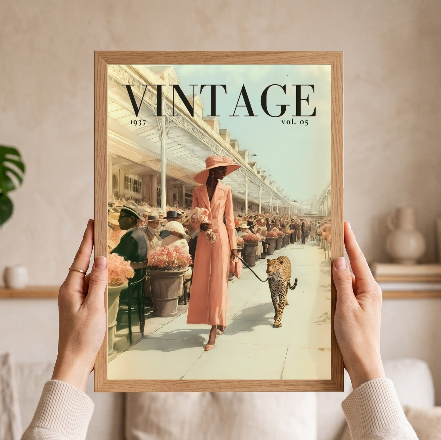 A person holds a framed art print featuring a vintage magazine cover design with the word 'VINTAGE' and an illustration of a woman walking a leopard on a terrace. The print is enclosed in a light wood frame, and the person's hands and sleeves are visible holding it against an indoor background.