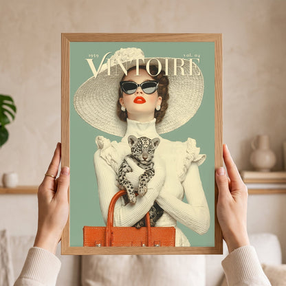 A person holds a framed vintage-style art print featuring a woman in a large hat and sunglasses holding a leopard cub, with the text 'VINTOIRE' and '1959 vol. 04' on a mint background.