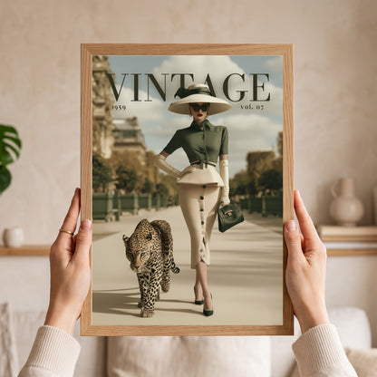 A person holds a framed vintage-style fashion poster in front of their torso. The poster shows a woman in a wide-brim hat and skirt walking with a leopard, with the word "VINTAGE" and "1959 vol.