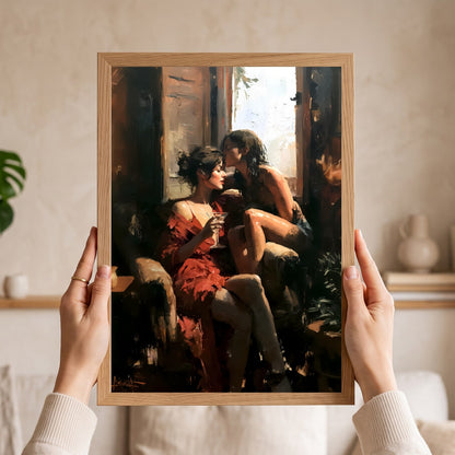 A framed art print depicting two women in a warm, sunlit interior, held up by two hands against a softly blurred home background.