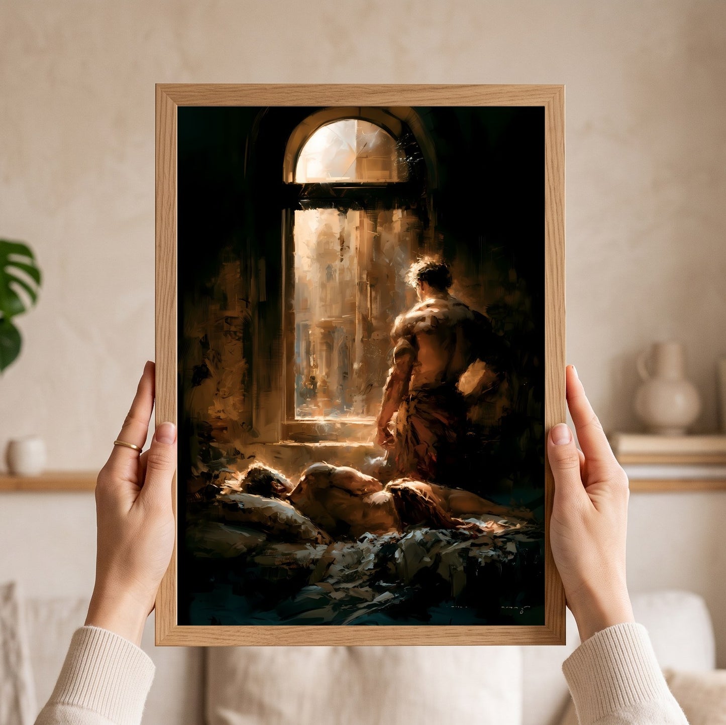 A person holds a framed art print featuring a classical painting of a figure looking out of a dark room toward a bright window. The print is shown in a light wood frame against a softly lit indoor background.
