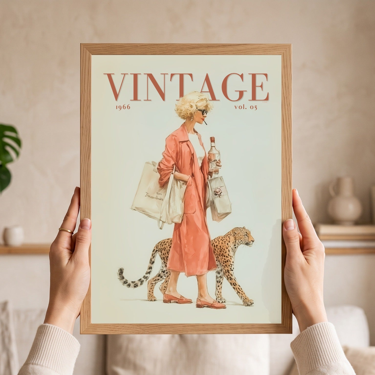A person holds a framed vintage-style art print featuring a woman in a peach dress walking beside a cheetah, with the word “VINTAGE” at the top. The print is shown in a light wood frame against a softly lit indoor background.