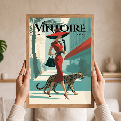 A person holds a framed vintage-style poster in both hands. The poster features an illustrated woman in a red dress and hat walking with a leopard, with the text 'VINTOIRE vol.