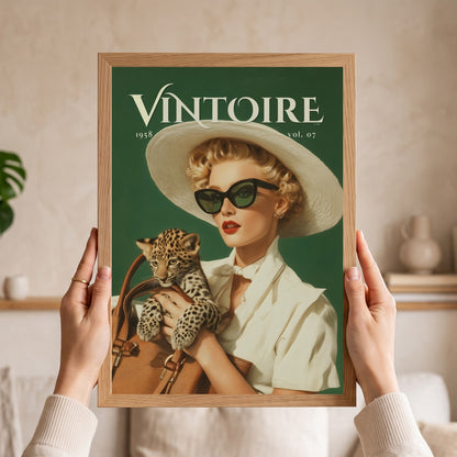 A person holds a framed art print featuring a vintage-style Vintore magazine cover with a woman in a white hat and sunglasses holding a leopard cub, against a softly blurred indoor background. Retro leopard wall art poster: 1950s woman in cat-eye sunglasses holding a leopard cub, green vintage print for maximalist decor