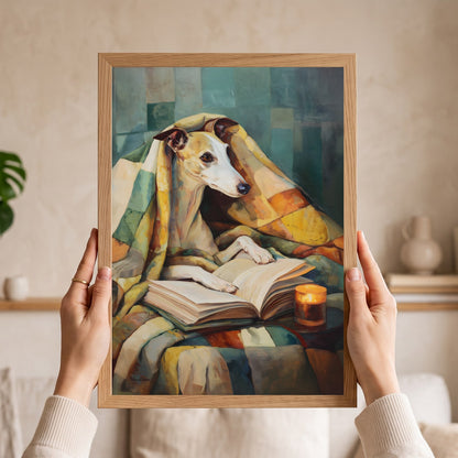 A person holds a framed art print featuring a stylized painting of a greyhound dog wrapped in a blanket and reading a book. The hands holding the frame are visible against a softly blurred indoor background with shelves and decor.