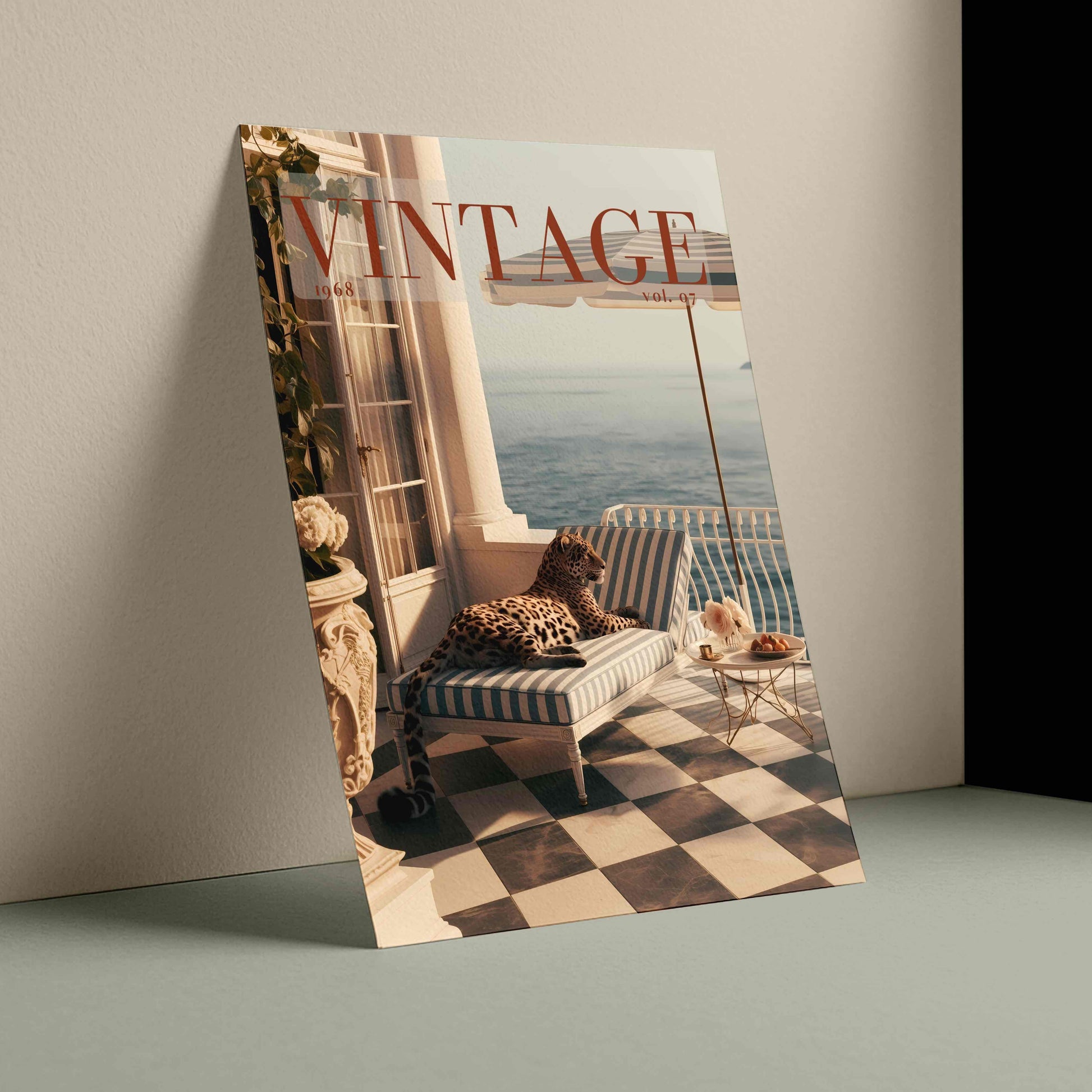 A magazine or book cover titled 'VINTAGE' leans against a beige wall on a muted green surface. The cover features a photograph of a striped lounge chair on a checkered balcony overlooking water, with a leopard resting on the chair.