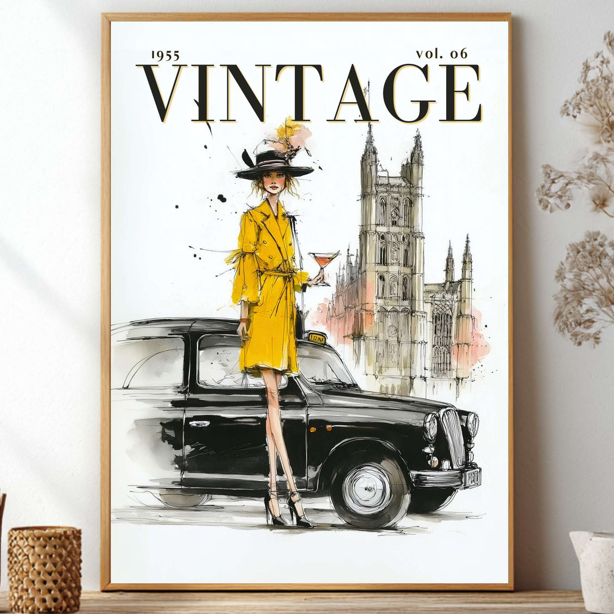 A framed vintage-style art print featuring a woman in a bright yellow coat and hat standing beside a black car, with a tower in the background and the word 'VINTAGE' at the top. The framed print is displayed on a shelf against a light wall with dried flowers and small decor items around it.
