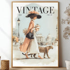 A framed vintage-style art print featuring a woman in a peach coat and white dress walking with a leopard, styled on a shelf beside dried flowers and decorative vases.