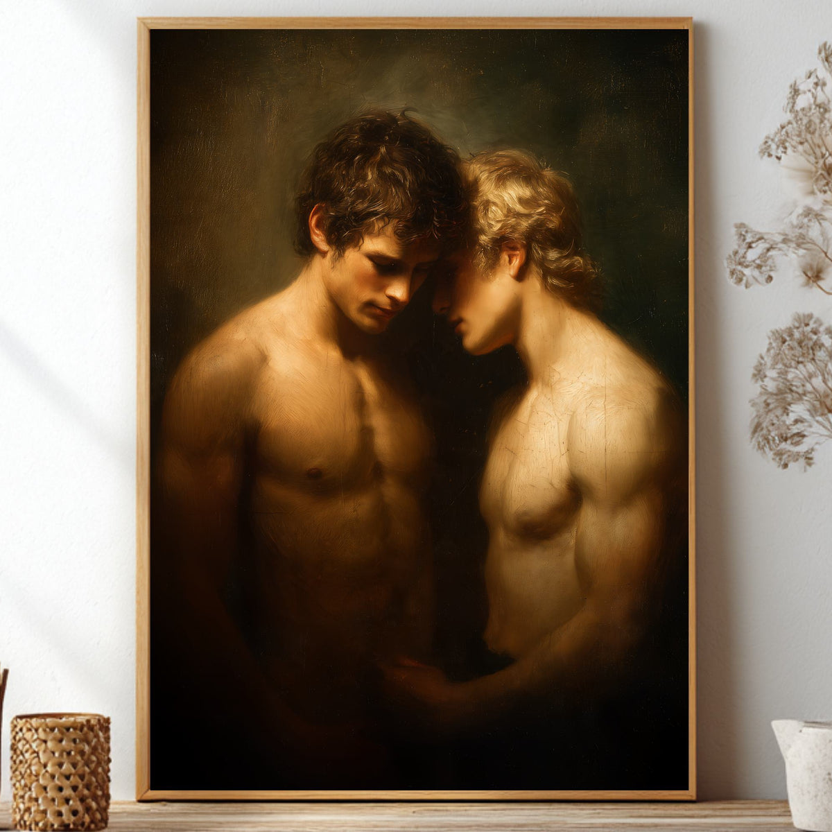 A framed classical-style painting depicting two shirtless male figures in a dimly lit, intimate pose, displayed on a shelf against a white wall with dried floral decor and small vases.