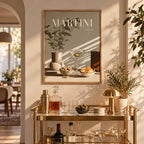 A framed art print featuring a martini still life with the text 'MARTINI vol. 10' hangs on a warm beige wall above a gold bar cart in a beautifully styled home bar setting.