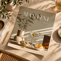 A styled flat-lay of a magazine or book titled "MARTINI vol. 10" on a sunlit beige tabletop.