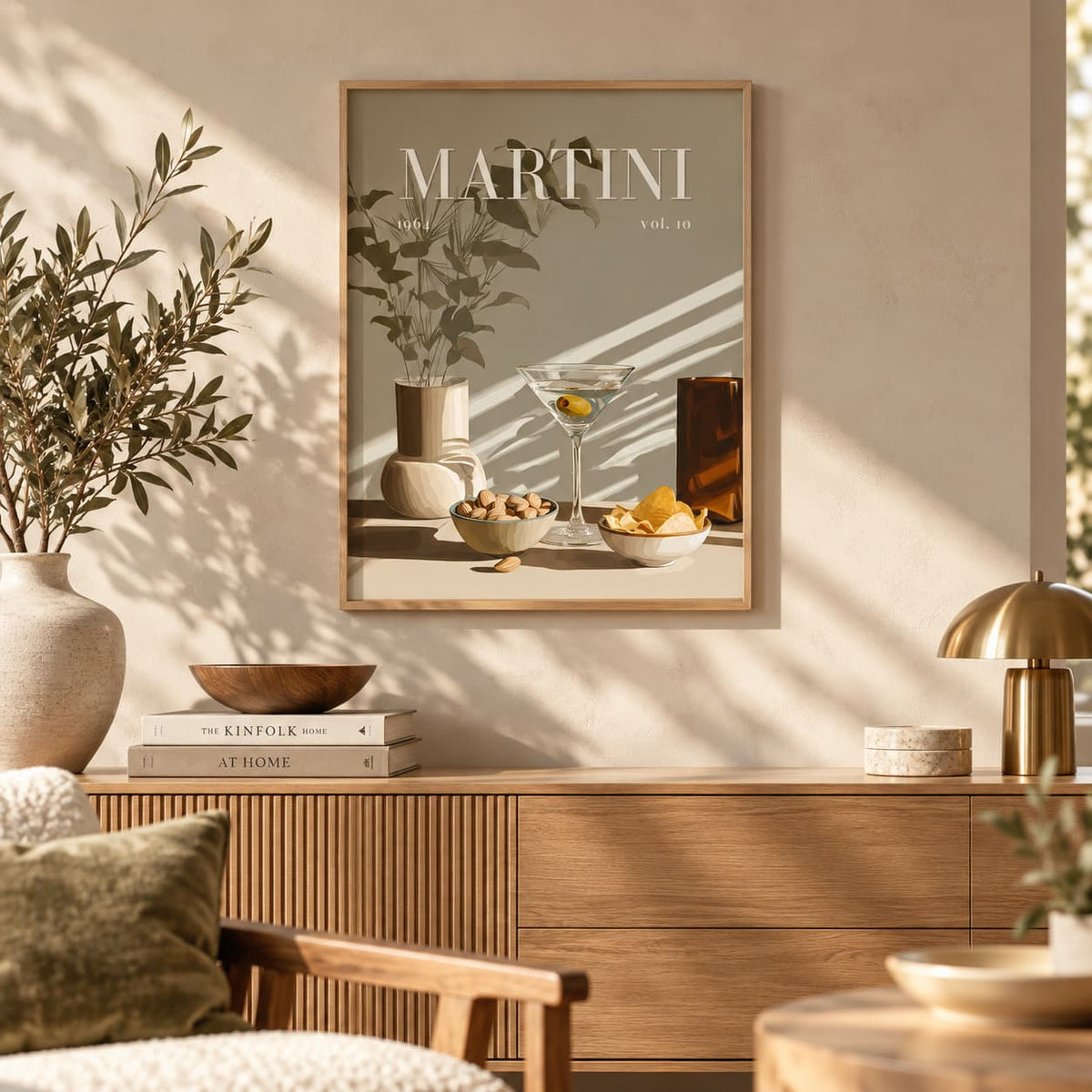 A framed art print featuring a vintage-style illustration of a martini cocktail and tableware, titled 'MARTINI vol. 10', displayed on a beige wall in a modern, sunlit living room above a wooden credenza.
