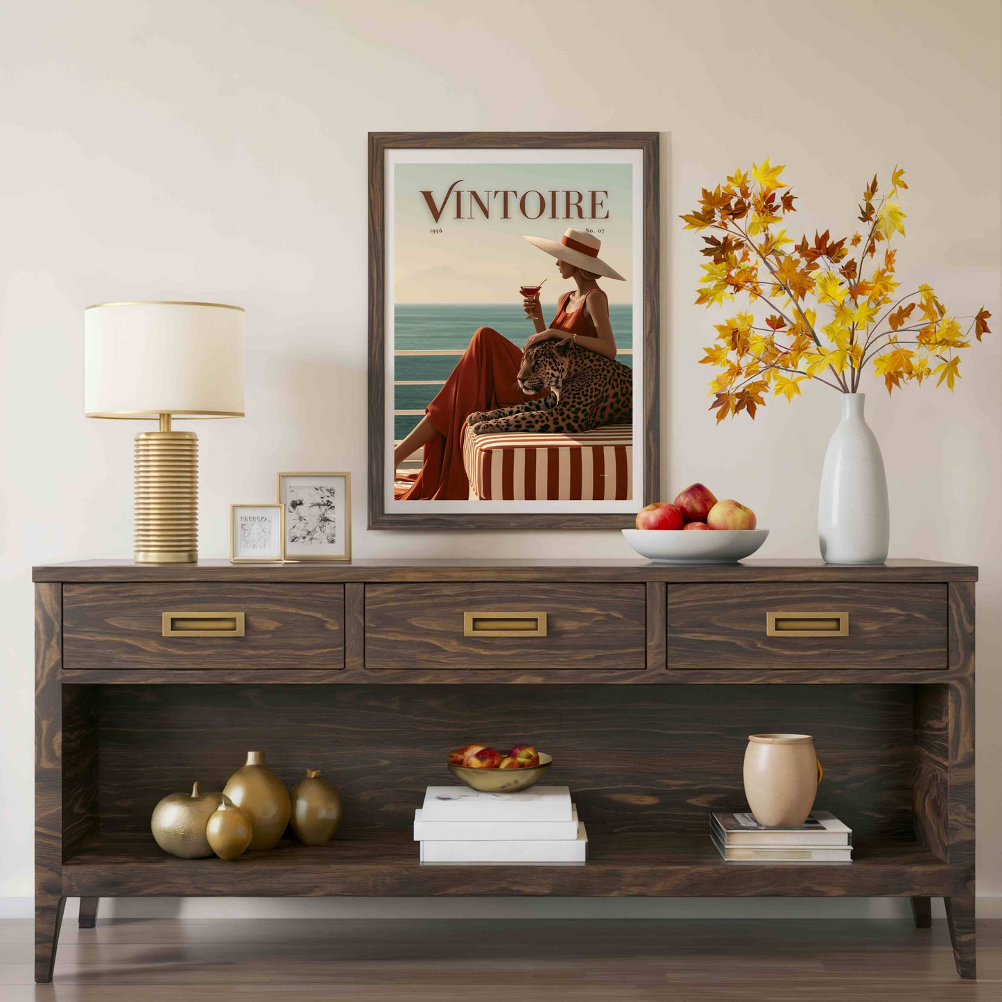 Wooden console table with decorative items including a framed poster, lamp, and vase. Framed poster of a faux magazine cover featuring a woman holding a cocktail with a leopard by the ocean, featuring the title 'Vintoire'.