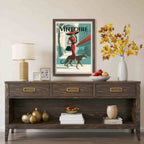 A framed vintage-style art print with the word 'VINTOIRE' hangs on a beige wall above a dark wood console table. The print shows a woman in a red dress and hat walking beside a leopard, with teal, cream, and red tones.