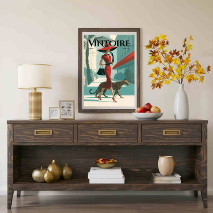 A framed vintage-style art print with the word 'VINTOIRE' hangs on a beige wall above a dark wood console table. The print shows a woman in a red dress and hat walking beside a leopard, with teal, cream, and red tones.